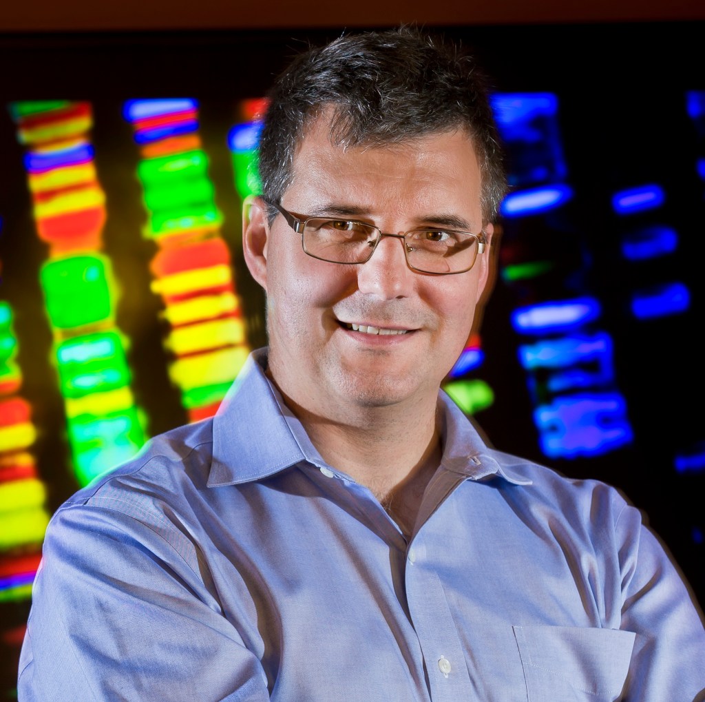 Portrait photo of man (Mihai Pop) wearing glasses, a blue button-down shirt set against a blurry multi-colored background.