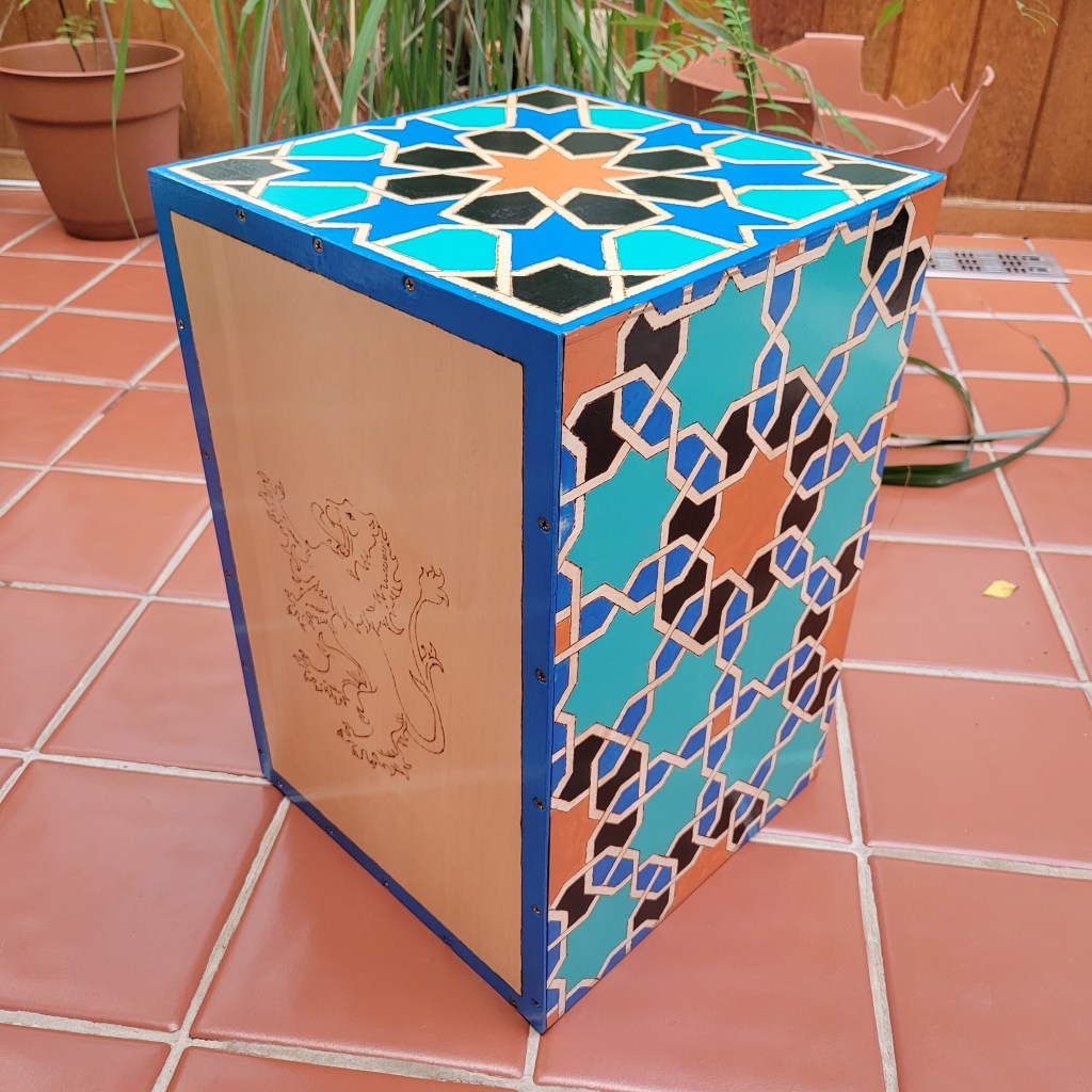 Wooden box with a plain front with a lion burned into it having a geometric pattern on the sides colored in various shades of blue and accented in orange.